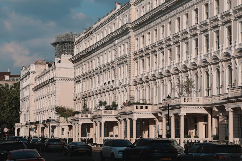 This image depicts a row of elegant Victorian-style townhouses with cream-colored facades, intricate architectural details, and prominent bay windows. The buildings feature decorative cornices, arched