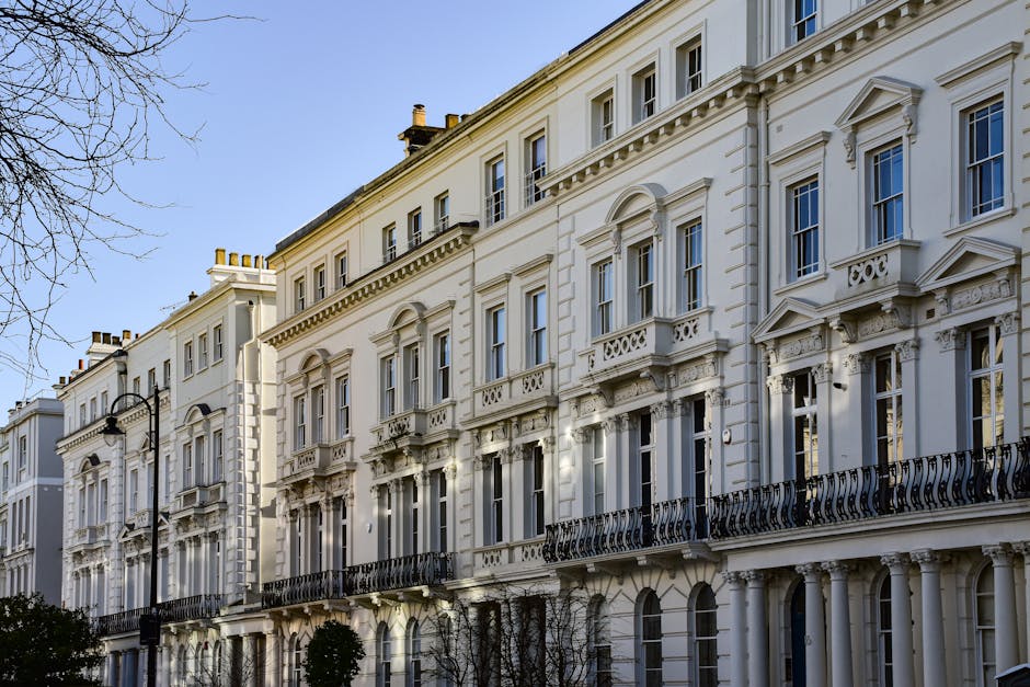 This image depicts a row of elegant Victorian-style townhouses with cream-colored facades, intricate architectural details, and prominent bay windows. The buildings feature decorative cornices, arched