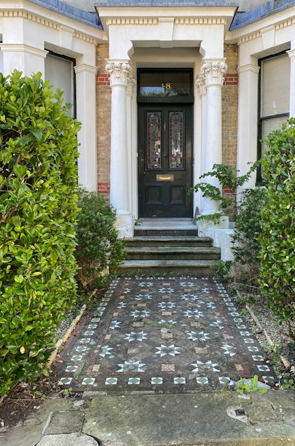A quiet residential street with a row of Victorian-style terraced houses, each featuring brick facades and chimney stacks, situated alongside a neatly maintained front garden area. The gardens display